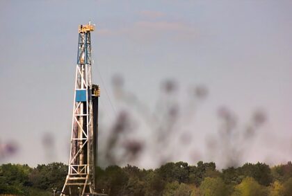 A blue and white fracking rig against a pale blue sky.