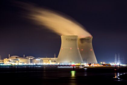 Two nuclear power cooling towers with steam rising against the night sky