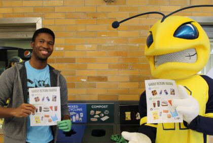 student poses with Rocky (a yellowjacket mascot) holding recycling posters