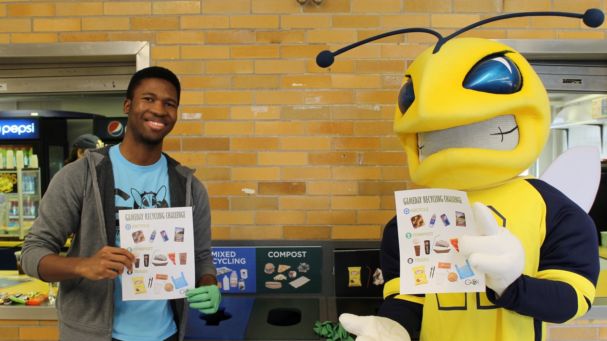 student poses with Rocky (a yellowjacket mascot) holding recycling posters