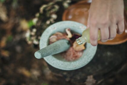 picture of a mortar and pestle with some herbs and the hand of a person pouring a liquid in to it also.
